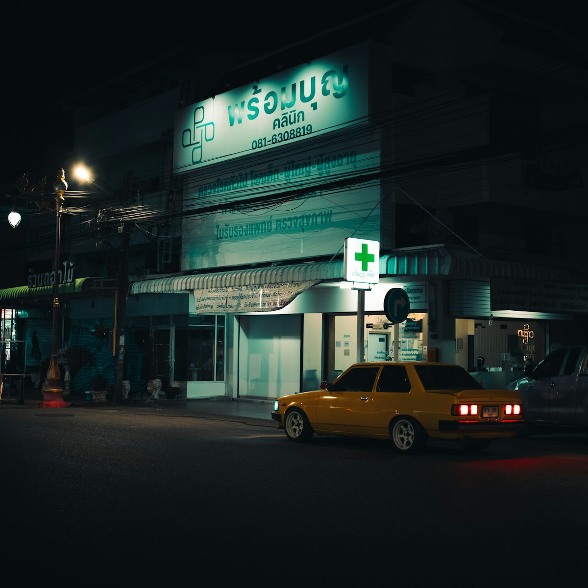 Yellow car parked outside a brightly lit pharmacy at night