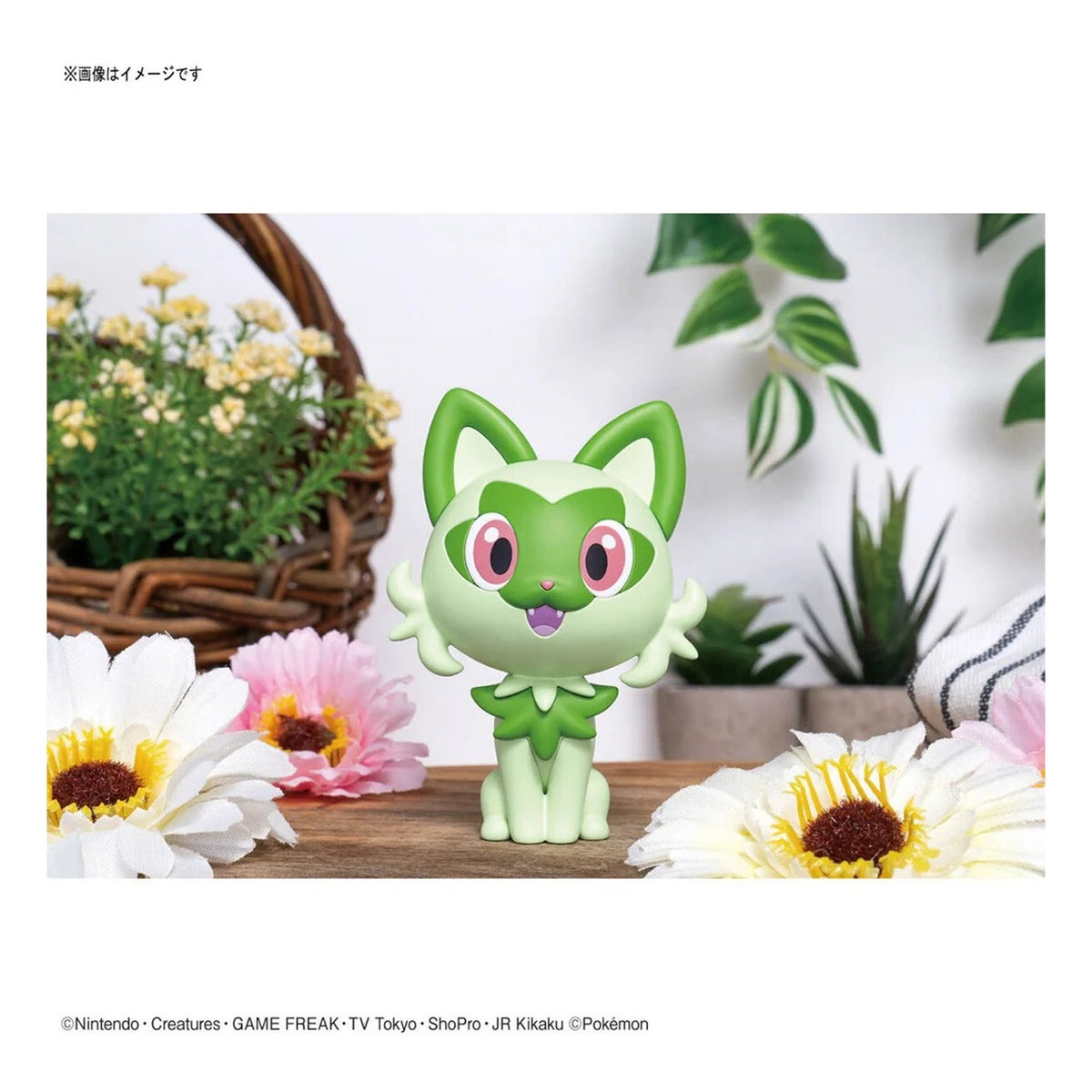 Completed Bandai Sprigatito Pokémon model kit displayed with flowers and green plants
